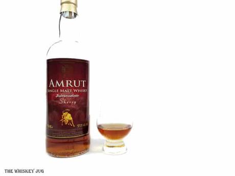 White background tasting shot with the Amrut Intermediate Sherry bottle and a glass of whiskey next to it.