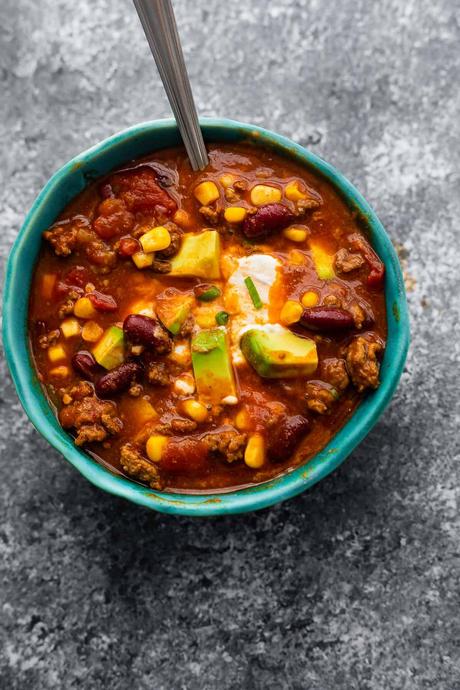 instant pot chili in blue bowl garnished with sour cream, cheese and avocado