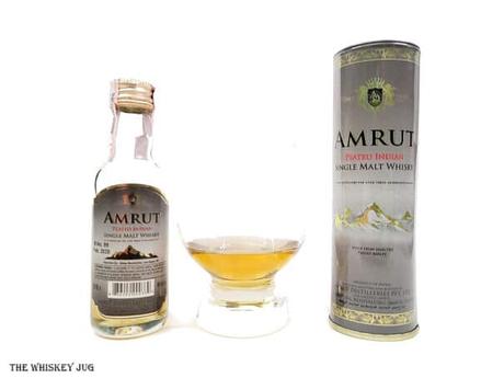 White background tasting shot with the Amrut Peated Indian Single Malt bottle and a glass of whiskey next to it.