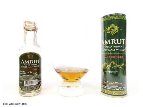 White background tasting shot with the Amrut Peated Cask Strength Indian Single Malt bottle and a glass of whiskey next to it.
