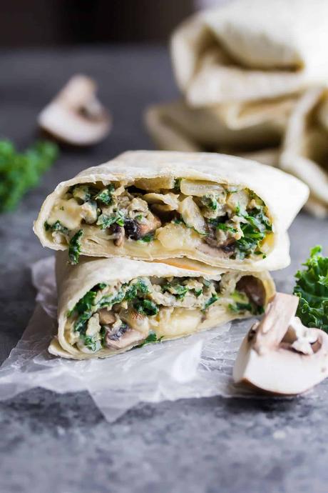 breakfast burrito with kale and mushrooms cut i half on parchment with fresh kale next to it