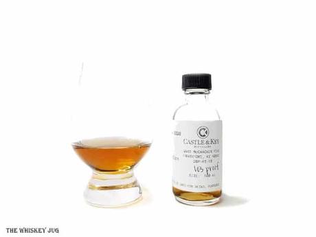 White background tasting shot with the Castle and Key Restoration Rye sample bottle and a glass of whiskey next to it.