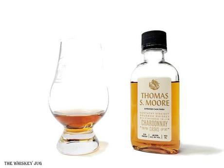 White background tasting shot with a sample bottle of the Thomas S. Moore Bourbon Chardonnay Casks L and a glass of whiskey next to it.