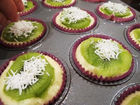 Uncooked muffins in trays, being topped with kiwifruit and coconut