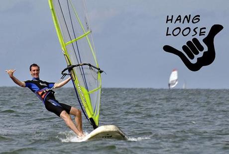 photo of man in wetsuit windsurfing and giving traditional Hawaiian hand signal for hang loose