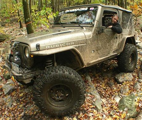 reference photo showing guy leaning out window of his mud-splattered jeep on rocky ground in forest