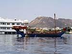 Wooden boat near the Jag Niwas Lake Palace and the Monsoon Palace in the background