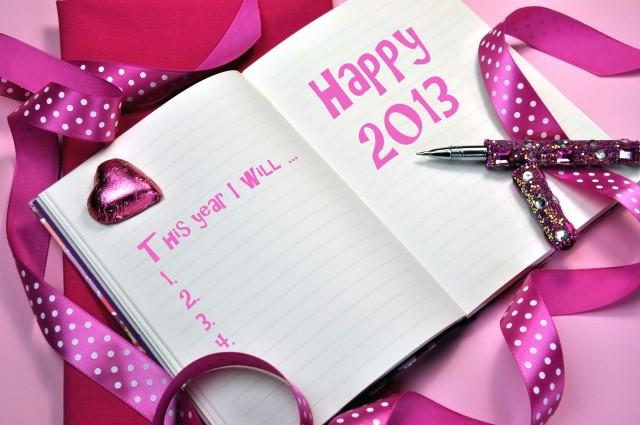 2013 Happy New Year message in pink diary with New Year Resolutions list on pink background with pink heart chocolate, polka dot ribbon and pink bling writing pen.