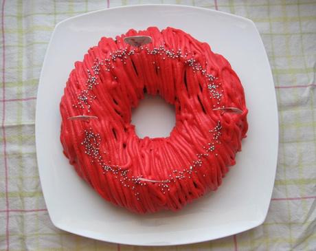 A round cake with red icing piped in lines with silver balls