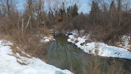 Water flows along snowy banks of a stream in the Claireville Conservation Area, in Toronto - Ontario