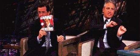 GIF of Jon Stewart and Stephen Colbert. Jon is dancing around adorably in his seat.