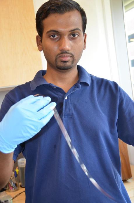Postdoctoral researcher Mohan Manoharan unspools a ribbon of 10-micron-thick flexible glass used to store energy. (Credit: Walt Mills, Materials Research Institute, Pennsylvania State University)