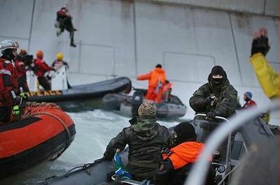 Russian Coast Guard officer, right, points a gun at a Greenpeace activist with raised hands, while another activist dangles on a rope from the Gazprom oil rig Prirazlomnaya, September 18, 2013 (Photo by Denis Sinyakov / Greenpeace)