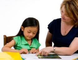 A young girl learns to write with the help of a teacher.