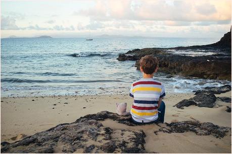 Boy watches ocean sitting next to stuffed sammy cat at papagayo beach in Lanzarote