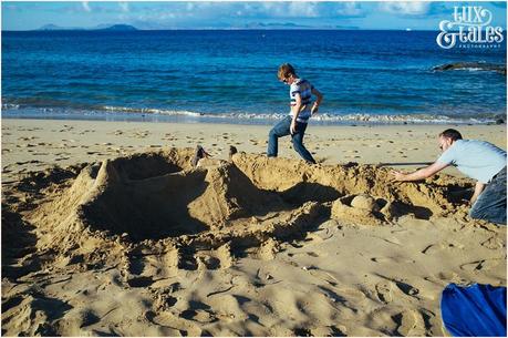 man and son build a sand castle at paapgayo beach in Lanzarote with boy stamping around in the background 