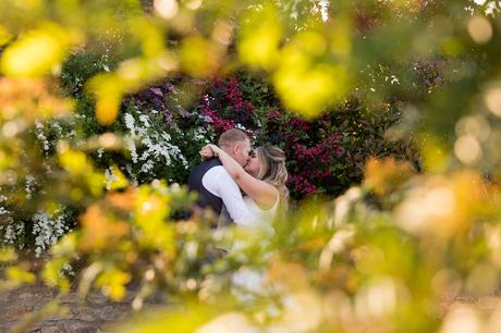 Bride & groom kiss sounded by colourful hedges