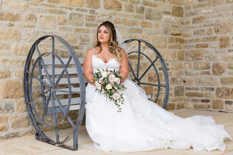 Bride sitting on a wagon wheel branch wearing a chunky lace dress