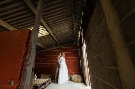 Wedding couple standing in front of an open barn door with a red wall behind them at Horseshoe Farm