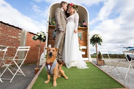 Bride Bride and groom standing in front of a mobile bar with their dog in the foreground