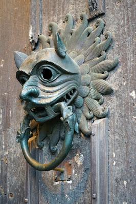 Photograph of the Durham Cathedral sanctuary knocker: a metal face, demonic in appearance, with a ring in its mouth, on a heavy wooden door.