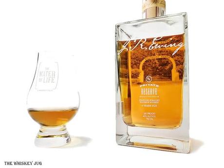 White background tasting shot with the J.R. Ewing Private Reserve Bourbon bottle and a glass of whiskey next to it.