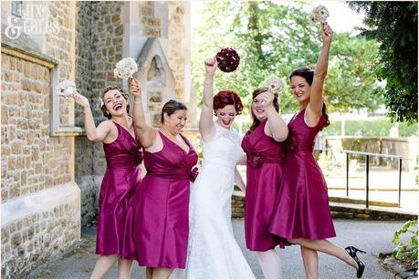 Red headed tattoo bride holds fabric bouquet in air with bridesmaids wearinf red