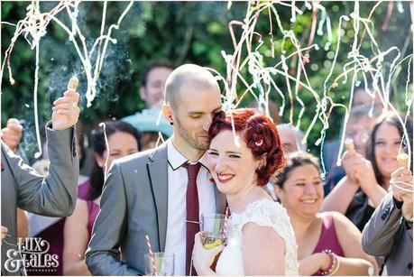 Red ehaded tattooed bride smiles at wedding party poppers photography