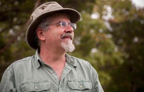 Man with hat in front of trees.