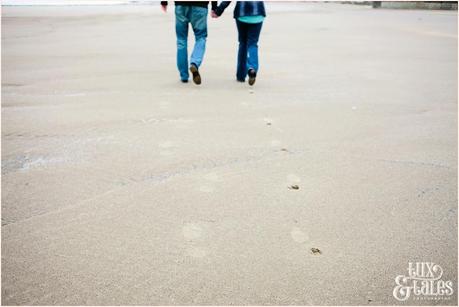 couple leaving footprints int he sand on beach