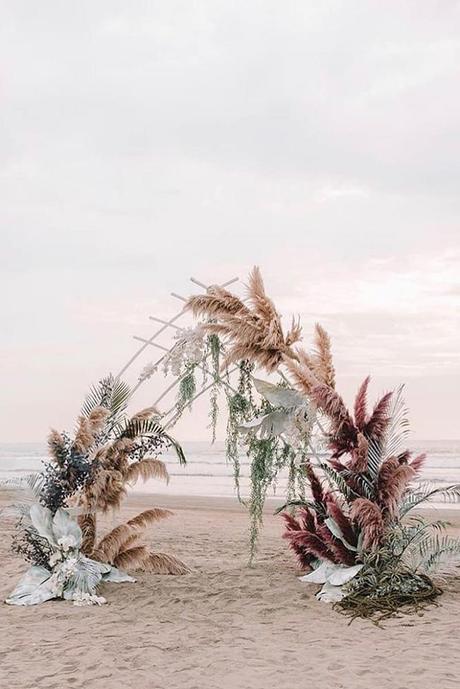 summer wedding trends bohemian beach ceremony with pampas grass and large leaves zhenyaswan