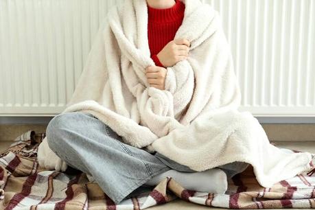 A woman sitting next to a radiator keeping warm in winter