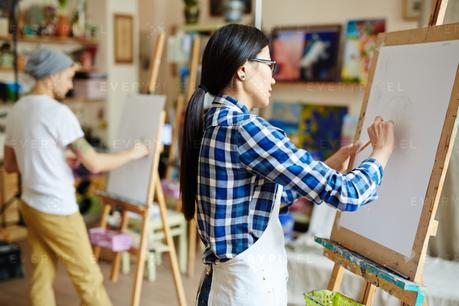 woman drawing on paper sheet on easel