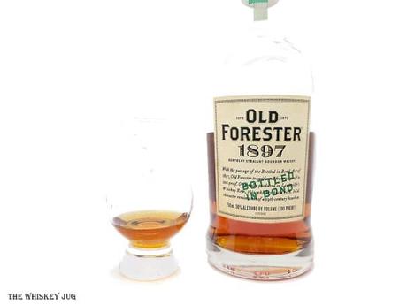 White background tasting shot with the Old Forester 1897 Bottled In Bond bottle and a glass of whiskey next to it.