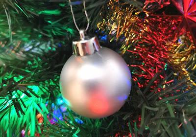 Illustrative photo of a bauble with tinsel and Christmas tree foliage in the background