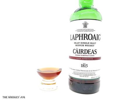 White background tasting shot with the Laphroaig Cairdeas 2021 Pedro Ximenez bottle and a glass of whiskey next to it.