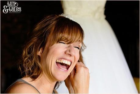 Bride laughs as she puts on her earrings in front of her wedding dress at New House Farm in the Lake District