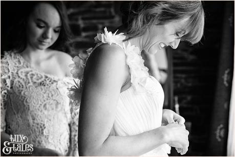 Bride mailes as she has her dress fastened at wedidng int he Lake district