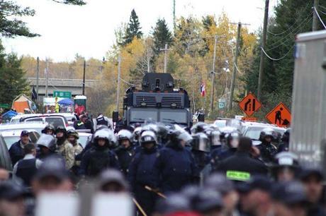 RCMP Tactical Armoured Vehicle lurks in the background behind riot cops, Oct 17, 2013.