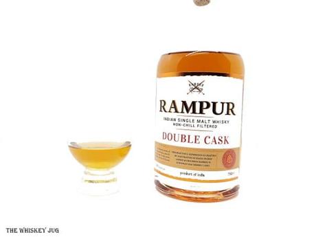 White background tasting shot with the Rampur Double Cask bottle and a glass of whiskey next to it.