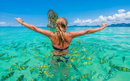 Enchanting Travels Asia Tours Woman swimming with snorkel surrounded by fish, Andaman Sea, Thailand