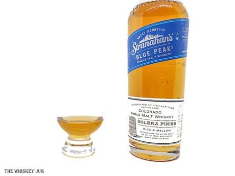 White background tasting shot with the Stranahan's Blue Peak bottle and a glass of whiskey next to it.