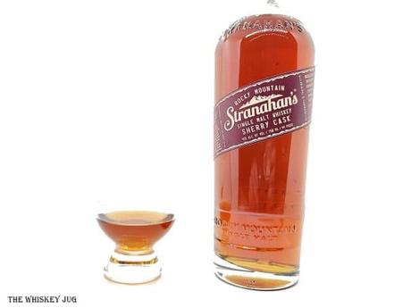 White background tasting shot with the Stranahan's Sherry Cask 008 bottle and a glass of whiskey next to it.