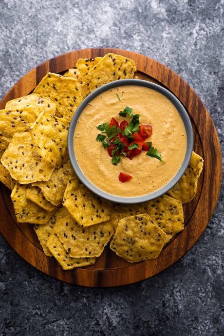 bowl of cashew queso topped with tomatoes and cilantro surrounded by chips