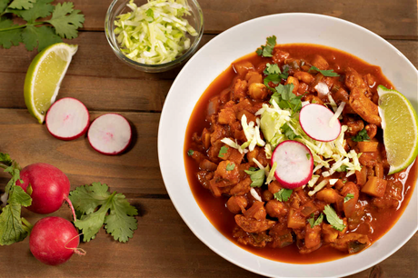 horizontal photo of a bowl of vegan possible with garnishes of shredded cabbage, radish, and lime