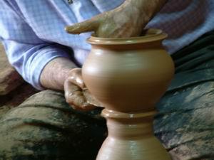 A man shapes pottery as it turns on a wheel. (...