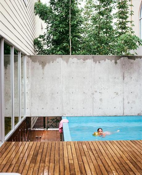Outdoor swimming pool by tall concrete fence and wood plank walkway