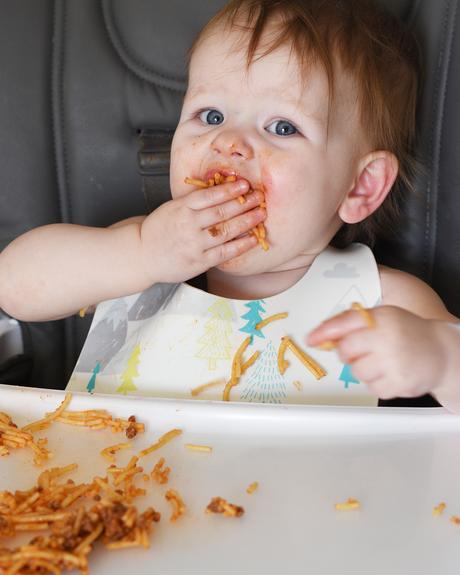 baby girl eating spaghetti in high chair