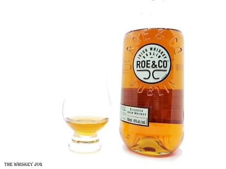 White background tasting shot with the Roe and Co Irish Whiskey bottle and a glass of whiskey next to it.
