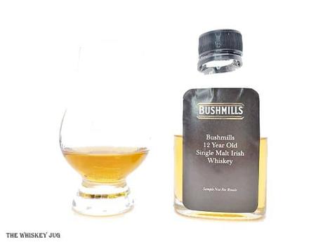 White background tasting shot with the Bushmills 12 Years Single Malt sample bottle and a glass of whiskey next to it.